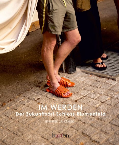 Text: "IM WERDEN Der Zukunftsort Schloss Blumenfeld JENNIFER JANOWSKI barton." Einige Personenfüße und Beine auf Kopfsteinpflaster.