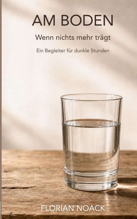„AM BODEN. Wenn nichts mehr trägt. Ein Begleiter für dunkle Stunden.“ Ein Glas Wasser steht auf einem Holztisch.
