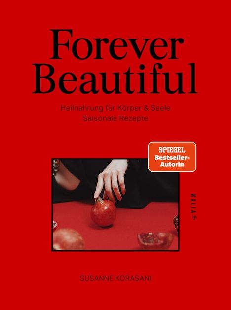 "Forever Beautiful", Heilmahrung für Körper & Seele, Saisonale Rezepte. Hand auf Granatapfel, roter Hintergrund.