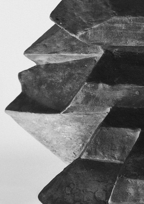 Große metallene Zacken einer Skulptur, dunkel und rustikal, wie ineinander greifende Zahnräder geformt.