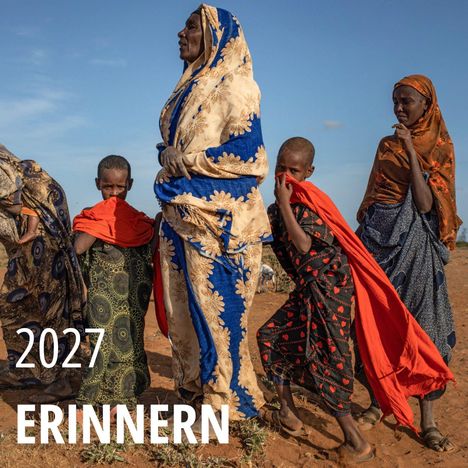2027 ERINNERN. Eine Gruppe von Menschen in bunten Gewändern steht in einer trockenen Landschaft.