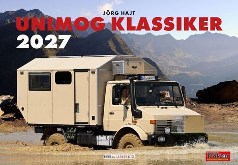 JÖRG HAJT UNIMOG KLASSIKER 2027. Ein beige Unimog fährt durch Wasser, umgeben von Berglandschaft.