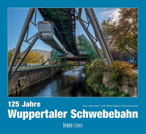 125 Jahre Wuppertaler Schwebebahn. Eine Schwebebahn fährt über einen Fluss, umgeben von grünem Laub.