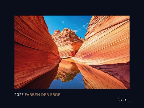 2027 FARBEN DER ERDE. Wellenförmige Felsen mit rot-orange Streifen, reflektiert in ruhigem Wasser unter blauem Himmel.