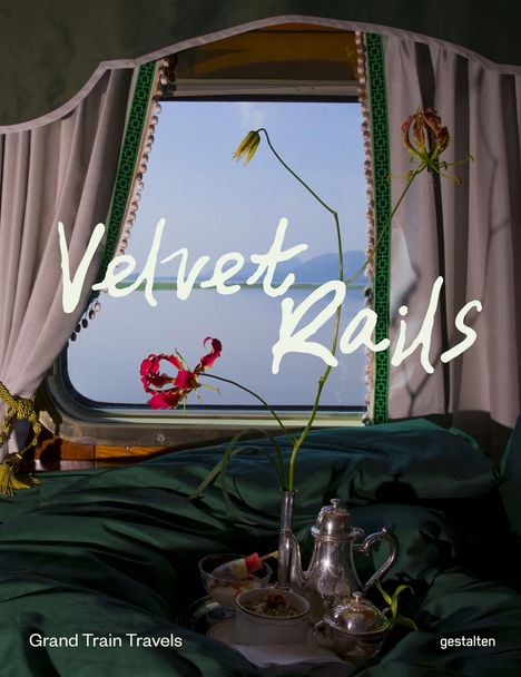 „Velvet Rails“ steht groß auf einem Fenster. Ein Teeservice und Blumen vor grünen Vorhängen in einem Zugabteil.