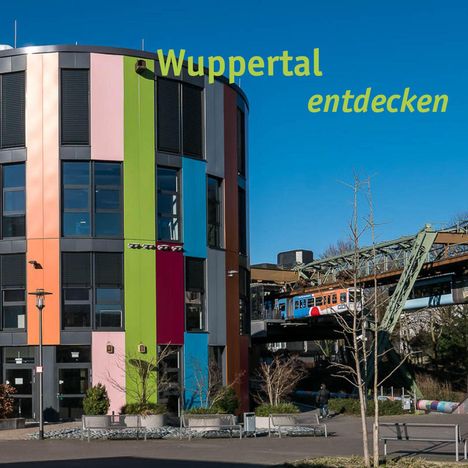 „Wuppertal entdecken“ in gelber Schrift, moderner Bau mit bunten Fassaden und Schwebebahn auf Stahlkonstruktion.