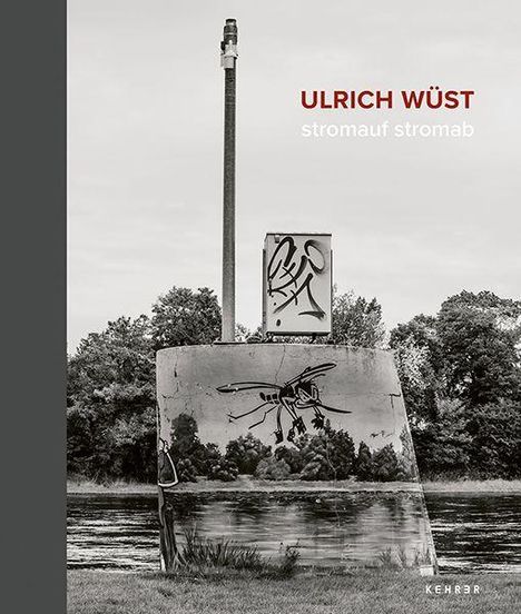 "ULRICH WÜST stromauf stromab" steht oben. Darunter ein Fluss, eine Betonwand mit Graffiti, Bäume im Hintergrund.