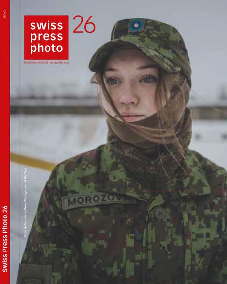 „swiss press photo 26“ in rotem Kasten. Junge Frau in Tarnuniform mit Mütze und Schal.