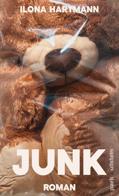 "ILONA HARTMANN", "JUNK", "ROMAN", "park x ullstein". Ein zerdrückter Plüschbär in Plastik verhüllt.