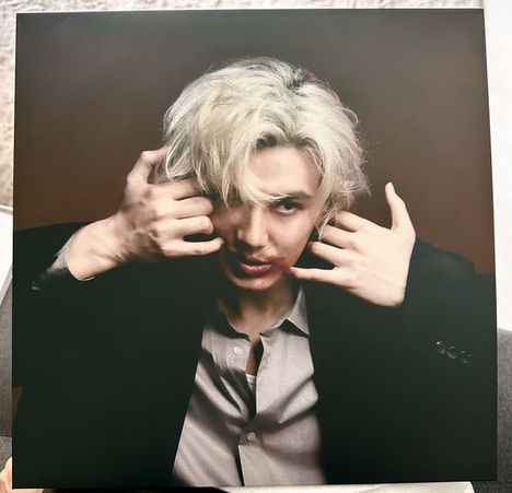 Es gibt keine sichtbaren Texte. Eine Person mit blondem Haar hält ihre Hände an den Kopf, trägt einen dunklen Anzug.