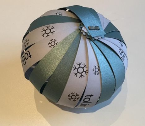 Text: "tolino" wiederholt. Papierkugel aus Streifen in Grün und Weiß mit Schneeflockenmuster.