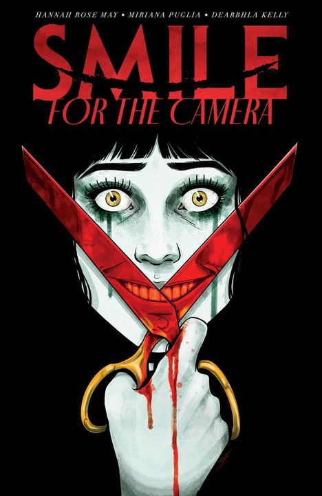 Text: „Smile for the Camera“. Frau mit gelben Augen hält rote Schere, die ihr Gesicht zu einem gezwungenen Lächeln formt.