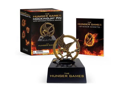Box: "The Hunger Games Mockingjay Pin." Sockel: "The Hunger Games." Buch: "The Hunger Games Sticker Sheets."