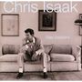 "Chris Isaak" oben, "Baja Sessions" rechts. Mann im Anzug sitzt nachdenklich auf einem Sofa, Bilder an der Wand.