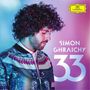Text: "Simon Ghraichy 33". Ein Mann mit lockigem Haar in bunter Jacke, vor pastellfarbenem Hintergrund.