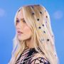 Keine erkennbaren Texte. Eine Frau mit blonden Haaren, darin blaue Sternensticker. Hintergrund in hellblau.