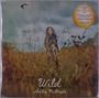 „Wild“ und „Ashley McBryde“ stehen unten. Eine Frau mit langem Haar steht in einem Feld, eine Krähe fliegt am Himmel.