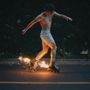 Kein Text vorhanden. Ein Mann in Shorts fährt auf Rollschuhen, Funken sprühen von den Rädern auf der dunklen Straße.