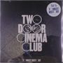 Text: "TWO DOOR CINEMA CLUB", "TOURIST HISTORY". Schwarzer Hintergrund, Katze im Bild, geometrisches Fliesenmuster.