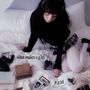 Text: "what makes a girl a girl". Eine Person mit Kopfhörern sitzt auf einem Bett, umgeben von Büchern und Fotos.