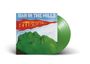 „MAN IN THE HILLS“ und „BURNING“ in lebhaften Farben über einer grünen Berglandschaft, grüne Vinyl-Schallplatte.
