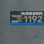 Texte: "Grand Master Gold", "Weezer", "1192", "Studio Mastering Audio Tape". Graue Oberfläche, schwarzes Rechteck, blaue Linie.