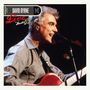Text: "DAVID BYRNE Live from Austin TX." Ein Mann singt in ein Mikrofon und spielt Gitarre. Konzerthintergrund.