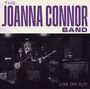 Text: "THE JOANNA CONNOR BAND" und "LIVE ON 11/11". Eine Band spielt auf einer Bühne mit Instrumenten.