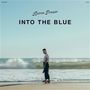 "Aaron Frazer - INTO THE BLUE." Ein Mann steht am Strand, blickt aufs Meer mit sanften Wellen und hellem Himmel.