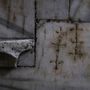 Eingravierte Kreuze auf rauem, hellgrauem Stein, rechteckige Platten, rustikale Struktur.