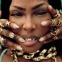 Text: Gucci-Logo auf einem Ring. 
Eine Person mit Goldschmuck, Nasenring und goldenen Grillz auf den Zähnen, Hände voller Ringe.