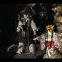 Eine Figur mit Fuchsmaske in einem bunten Kimono, daneben ein Puppenwesen mit Strohhut in dunkler Umgebung.