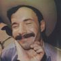 Ein Mann mit Schnurrbart und Cowboy-Hut lächelt, während jemand sein Gesicht sanft hält.