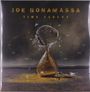 "JOE BONAMASSA TIME CLOCKS." Eine kaputte Sanduhr in einer kargen Landschaft, mit verstreutem Sand und Scherben.