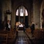 "Hallan What's a Heaven For?" - Eine Gruppe von Personen steht in einer düsteren Kirche mit hohen Decken und Buntglasfenstern.