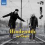 „Hindemith in Paris“ in Gelb. Zwei fröhliche Männer auf Bahngleisen. Einer balanciert, der andere hält eine Posaune.