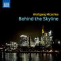 Text: "Wolfgang Mitschke Behind the Skyline." Nachtszene einer beleuchteten modernen Skyline am Wasser. Logo oben links.