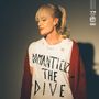 Texte: "ROMANTICIZE THE DIVE". Eine blonde Frau mit Pony trägt ein zerrissenes T-Shirt und eine rote Strickjacke.