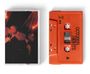 Ein leuchtend orangefarbenes Kassettenband mit "OCTOBER NIGHTS" und "OCTOBER LONDON". Daneben ein dunkelrotes Foto.