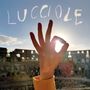 Text: "LUCCIOLE" in Wolkenoptik. Eine Hand formt ein "OK"-Zeichen, die Sonne scheint durch den Kreis, im Hintergrund Ruinen.