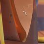 Keine erkennbaren Texte. Abstrakte Skulptur mit geschwungenen, orange-braunen Flächen und einem kleinen, silbernen Detail.