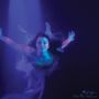 "Maiah Wynne Into The Waves". Eine Frau schwebt in blauem Licht im Wasser, umgeben von sanften Bewegungen und blauen Tönen.