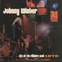 Text: Johnny Winter, Live at The Fillmore East 1970.  
Szene: Ein Musiker spielt Gitarre auf einer beleuchteten Bühne.