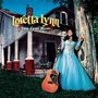 „Loretta Lynn, Van Lear Rose.“ Frau in blauem Kleid lehnt an Baum, Gitarre vor altem Haus mit Säulen.