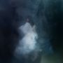 Ein verschwommenes, mystisches Bild; eine Figur in Weiß bewegt sich durch dichten, dunklen Nebel.