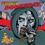 „OPERATION: DOOMSDAY.“ Ein Mann in einer Maske und Kapuze hält ein Mikrofon, hinter ihm rauchen Gebäude. Comicstil.