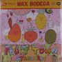 "WAX BODEGA" oben, "FRUIT TOWN STANDARDS" unten. Illustration von fröhlichen Früchten mit Gesichtern auf rosa Hintergrund.