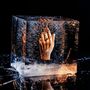 Kein Text sichtbar. Eine Hand mit Ring ist in einem klaren Eisblock eingeschlossen, umgeben von Luftblasen.