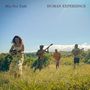 Text: "Mia Doi Todd HUMAN EXPERIENCE". Vier Personen spielen Instrumente auf einer Wiese an einem sonnigen Tag.