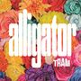 "alligator TRAM" steht in großen, weißen Buchstaben vor einem bunten Hintergrund aus verschiedenen Blumen.